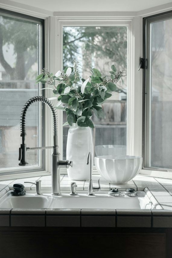 Kitchen sink with a large vase of greenery in front of a bay window.