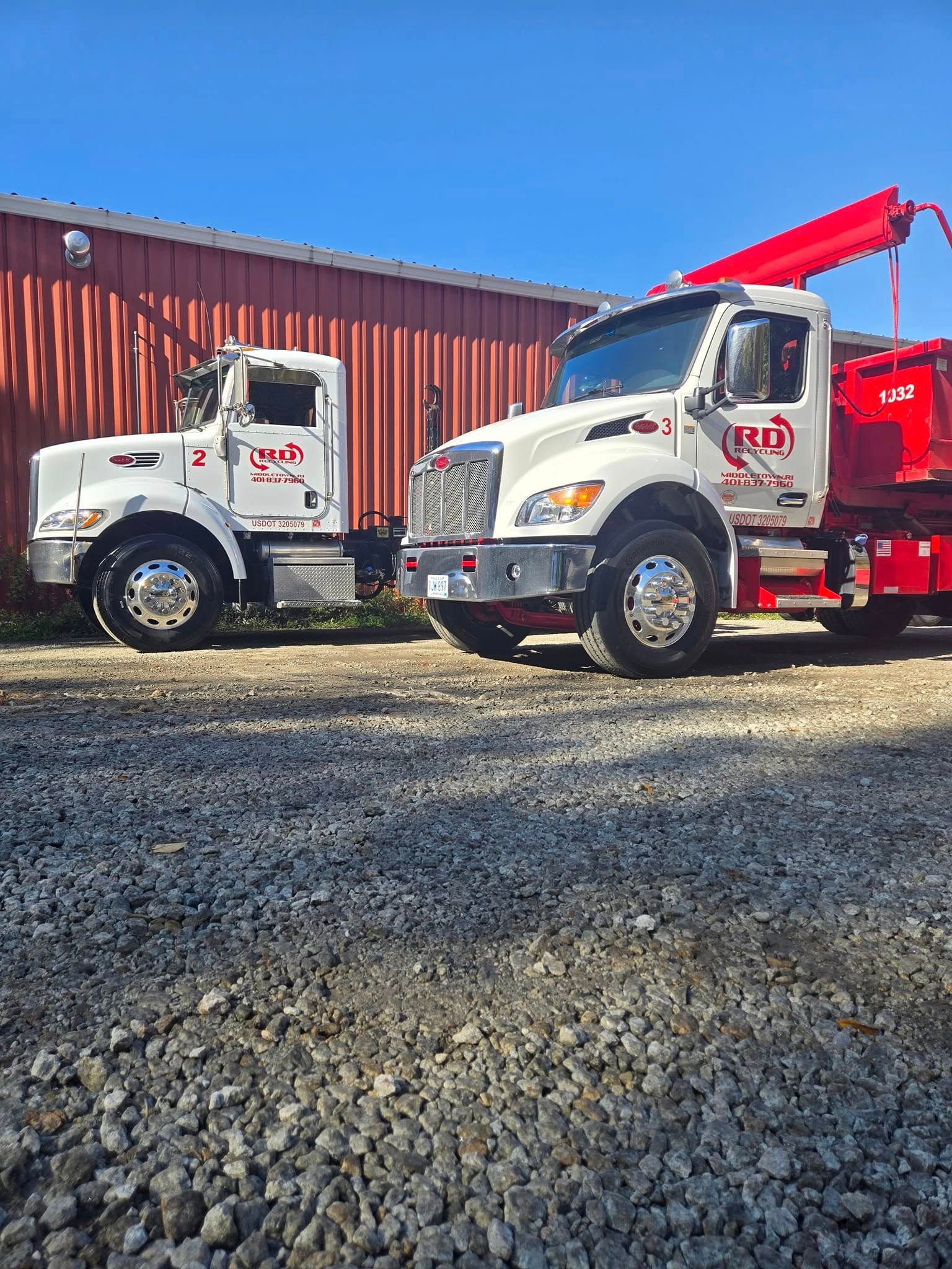 Two white red tow trucks parked on gravel in front of a red building under a blue sky