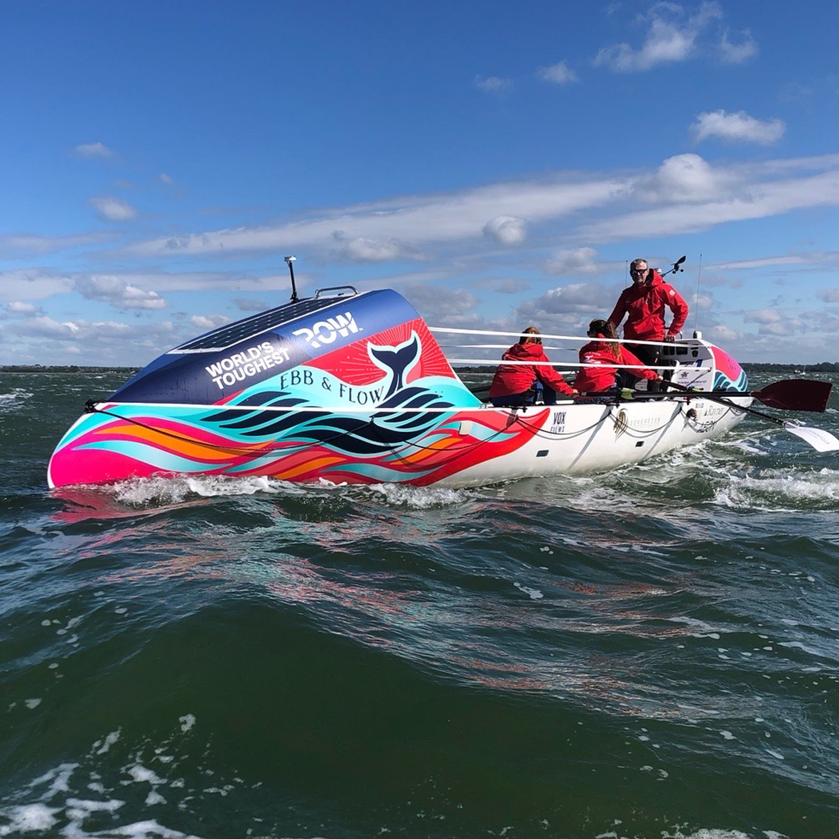 Colorful rowboat with three people in the open water under a blue sky.