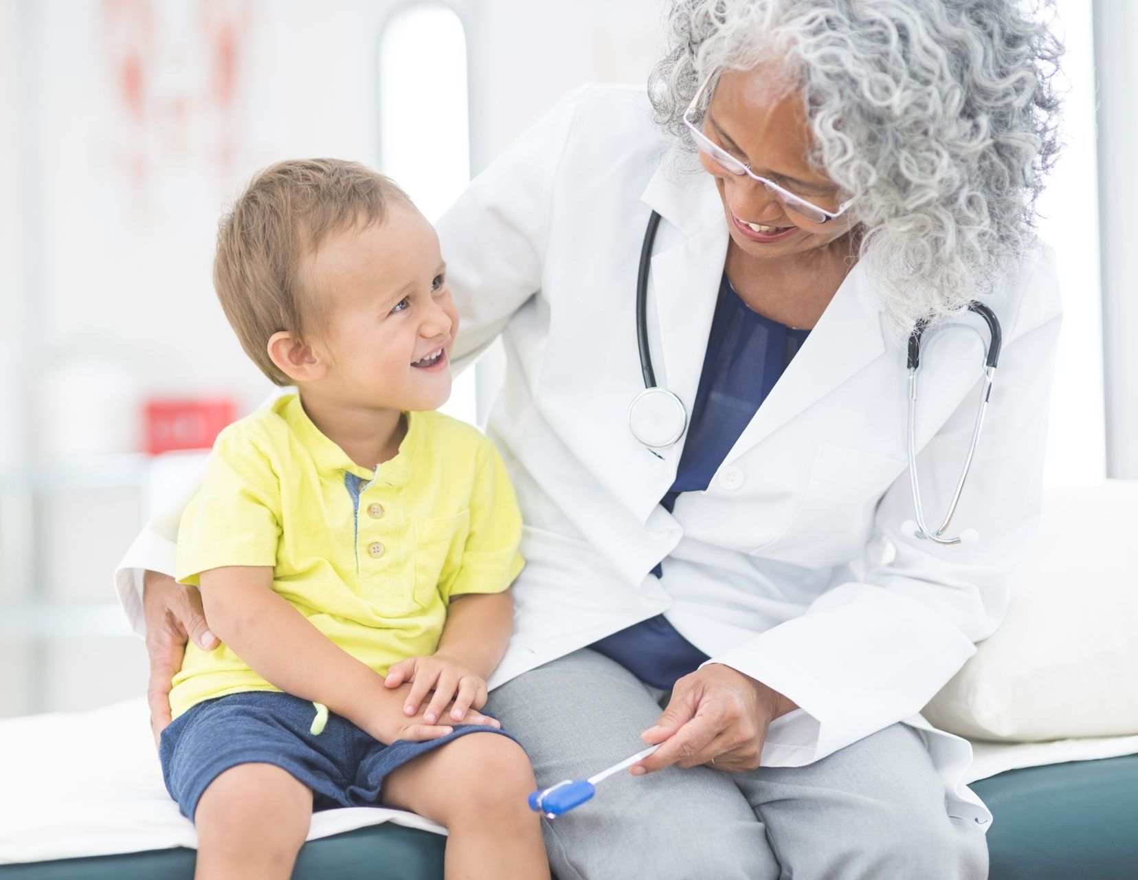 A doctor is examining a young boy 's knee with a thermometer.