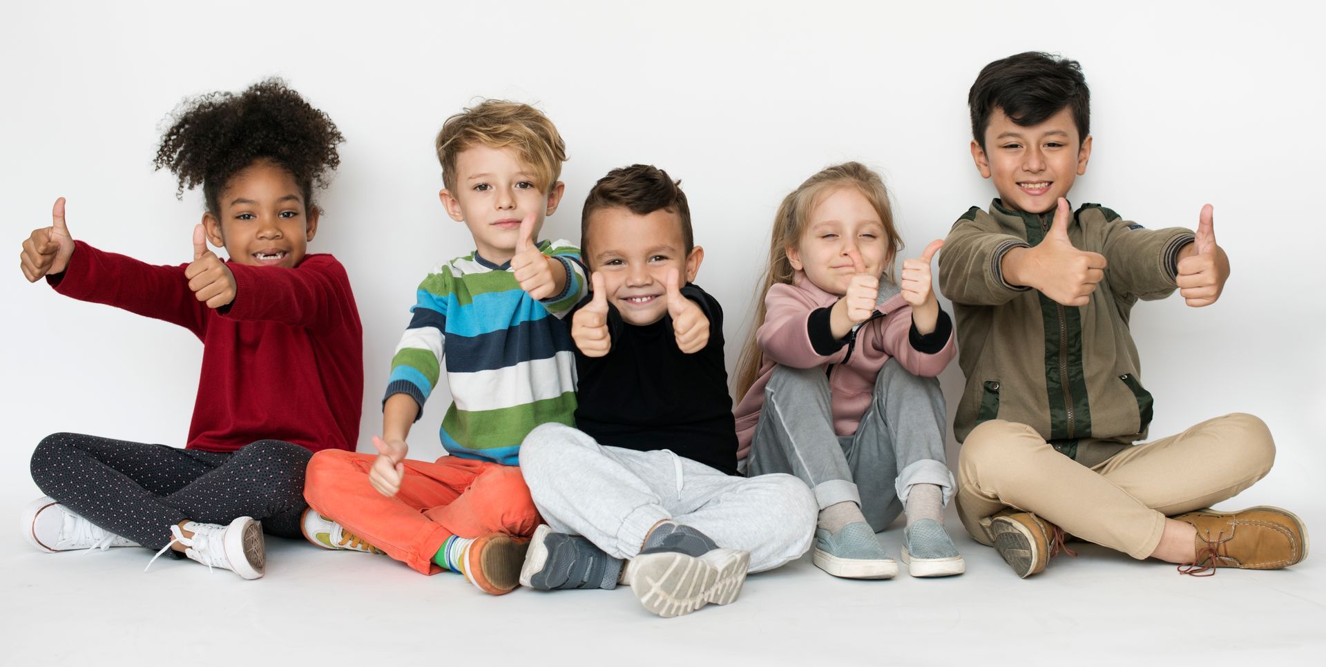 A group of children are sitting on the floor giving thumbs up.