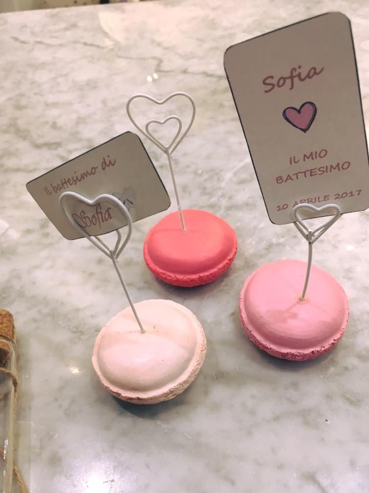 Tre macaron rosa con bigliettini attaccati su un tavolo.