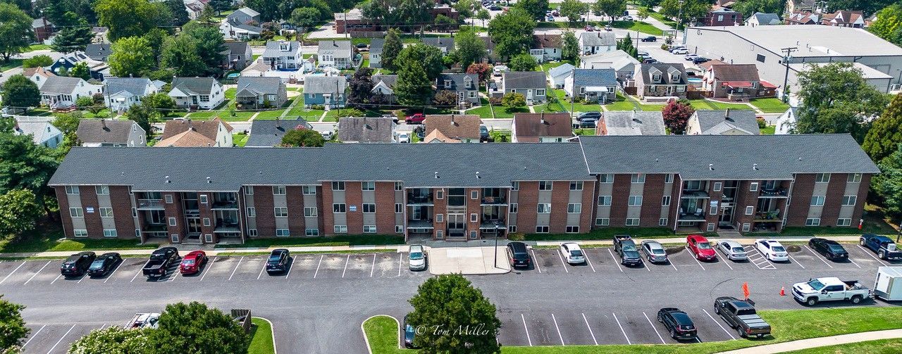 Aerial view of a long brick apartment building with parked cars and trees in a residential area