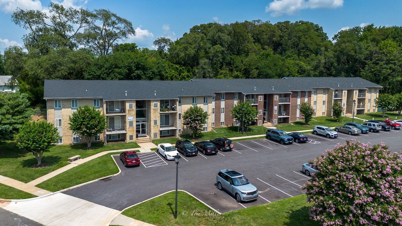 Aerial view of a two-story apartment building with parked cars and trees surrounding the lot.