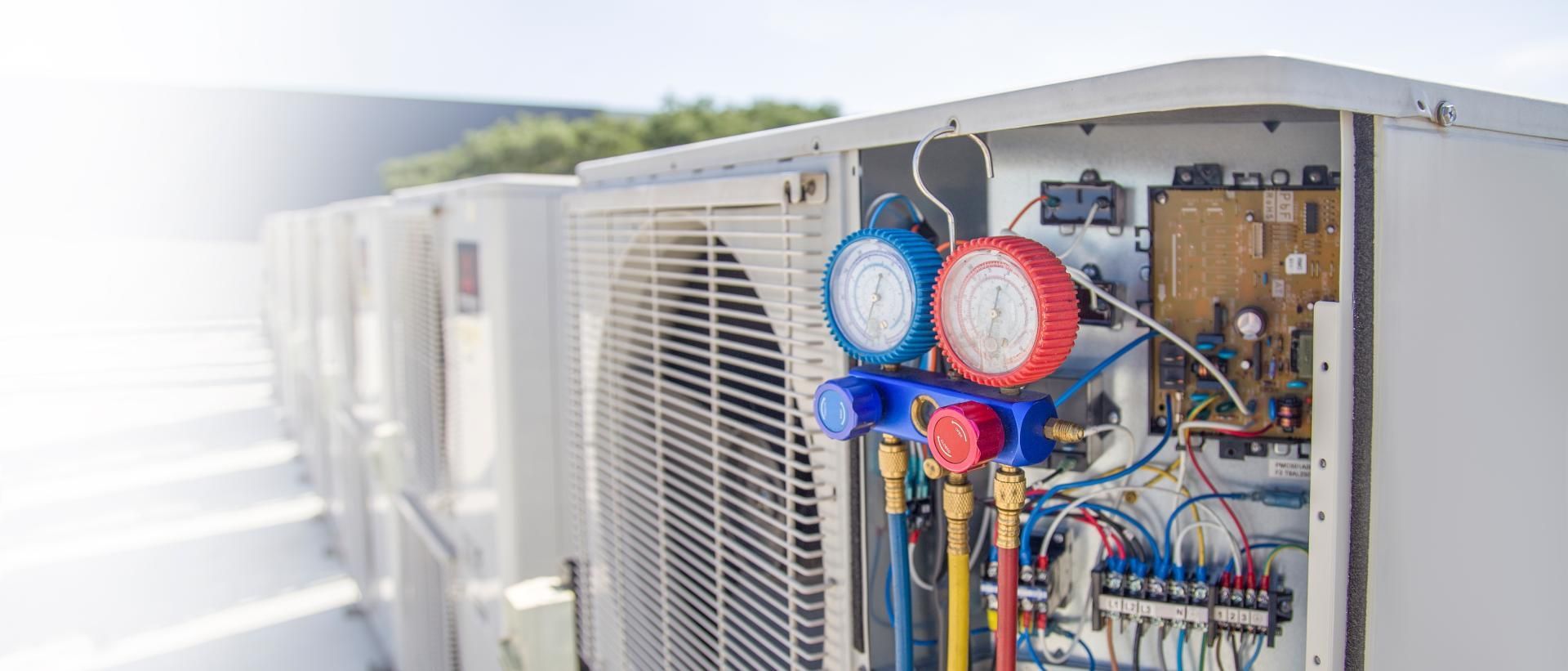 HVAC unit being serviced with gauges, visible wires, and tubing; outdoors.