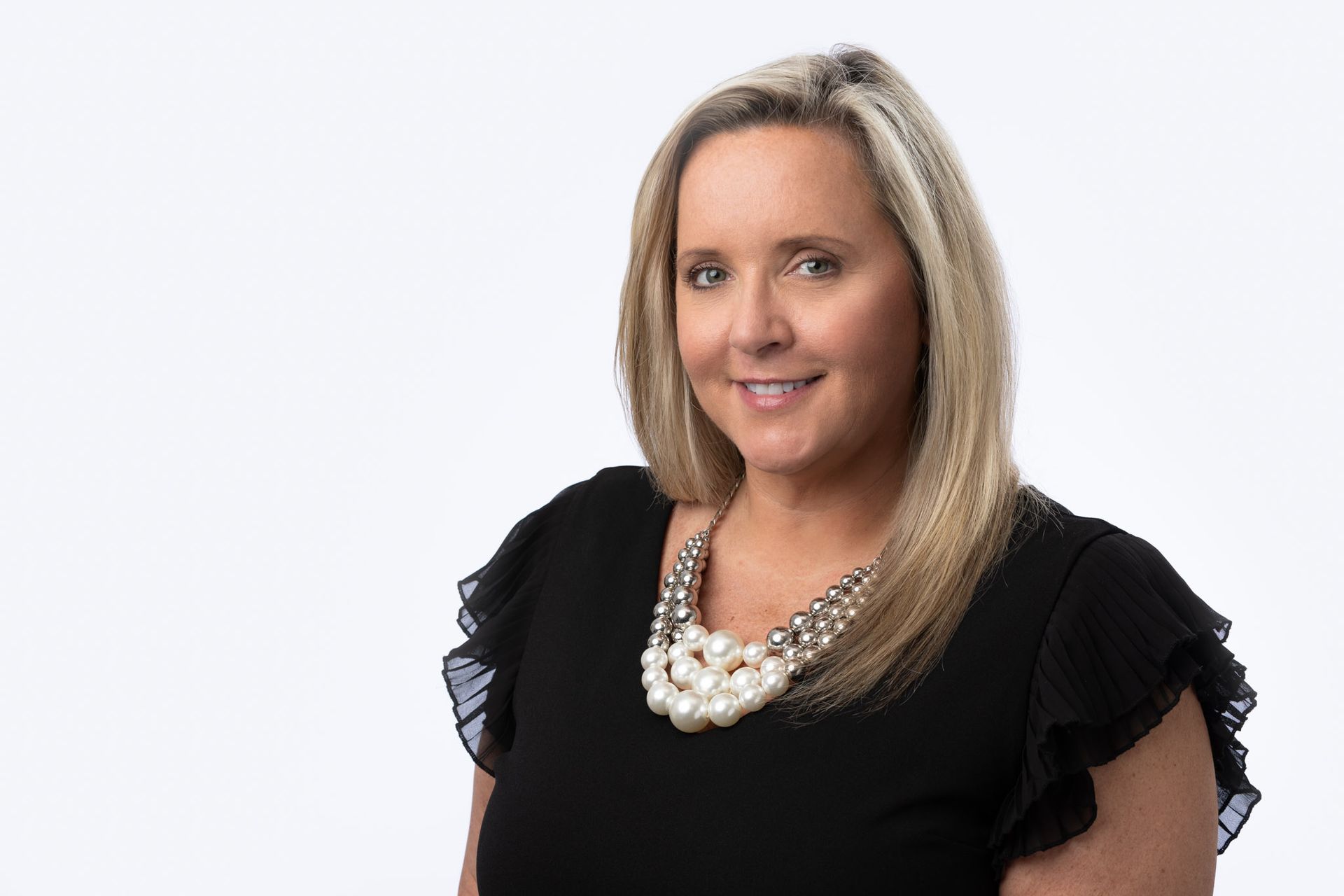 A woman wearing a black shirt and a pearl necklace is smiling for the camera.