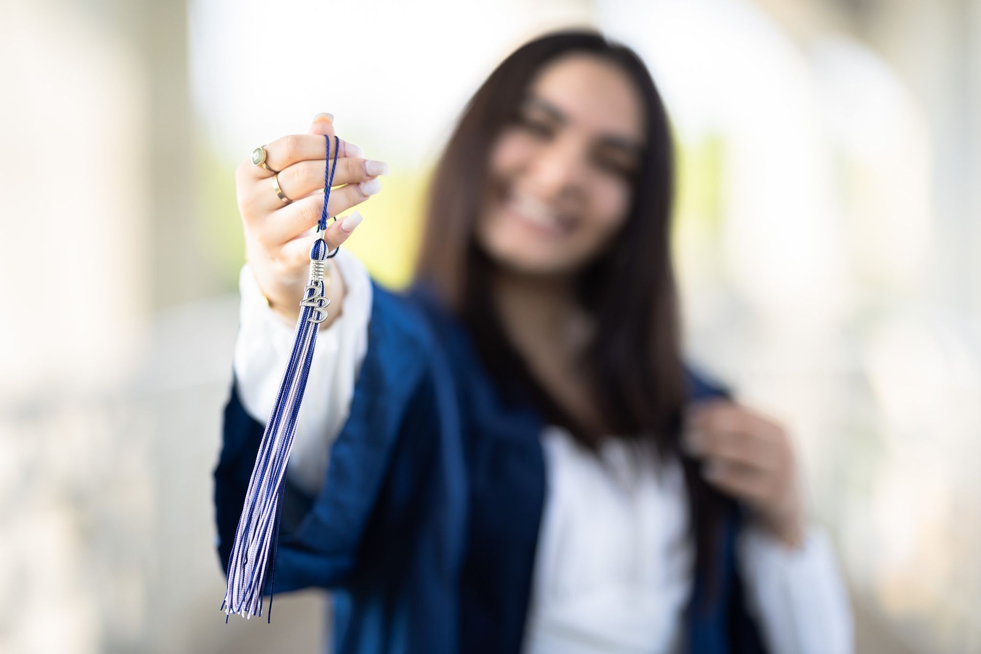 A woman in a graduation cap and gown is holding a blue tassel.