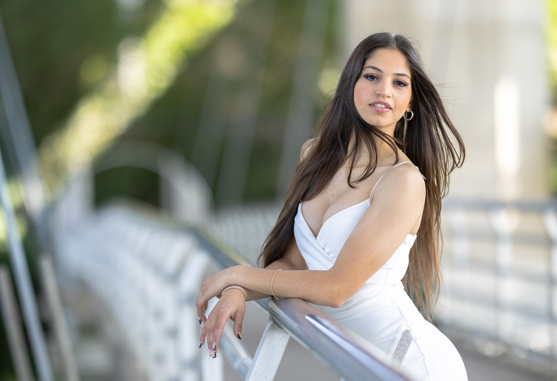 A woman in a white dress is leaning on a railing on a bridge.
