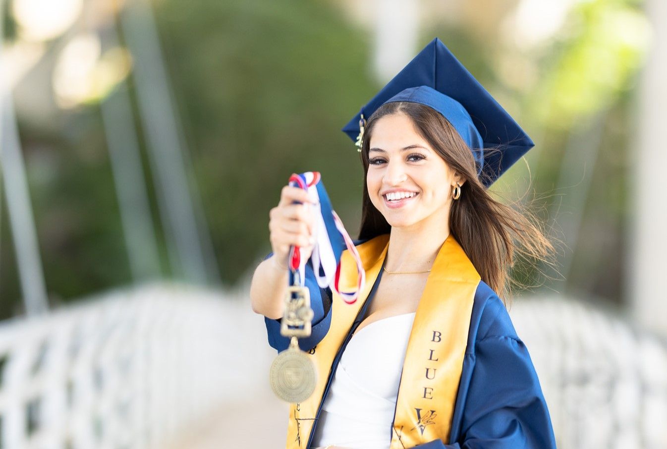 A woman in a graduation cap and gown is holding a medal