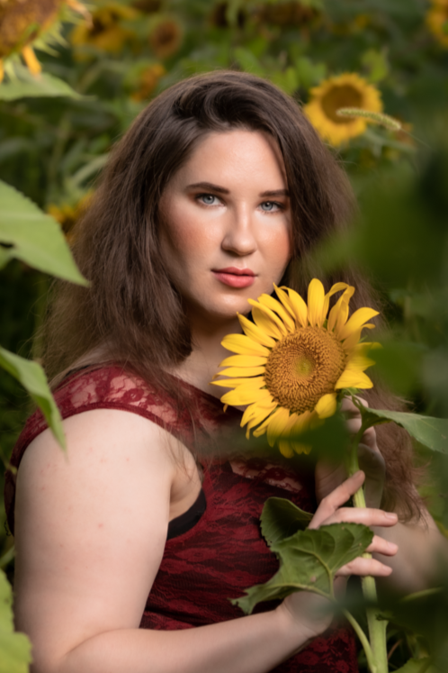 A woman in a red dress is holding a sunflower in a field of sunflowers.