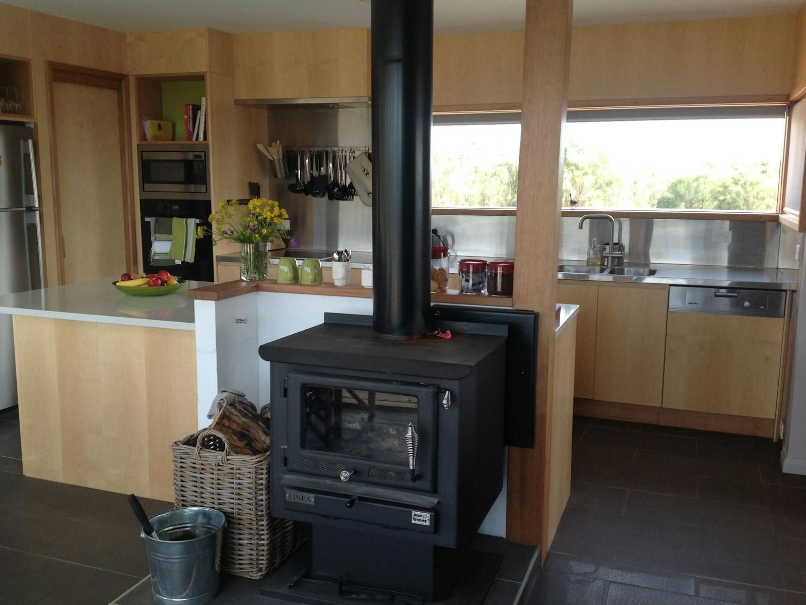 Kitchen With a Black Wood Stove, Light Wood Cabinets, and a Bright Window — Complete Heating In Huntingfield, TAS