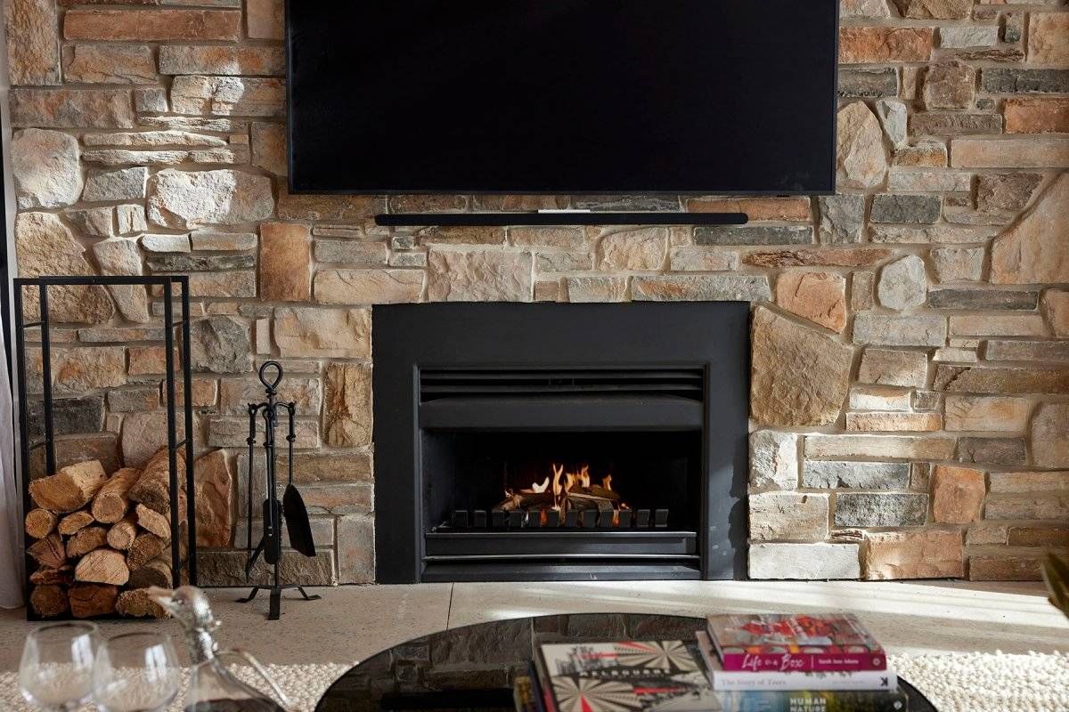 Stone Fireplace With a TV Above It and Stacked Firewood — Complete Heating In Huntingfield, TAS