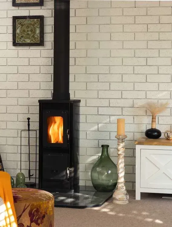 Living Room With a Lit Wood Stove, Brick Wall, and Decorative Vases and Cabinet — Complete Heating In Huntingfield, TAS
