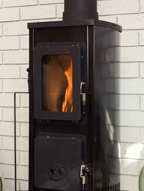 Black Wood Stove With Orange Flame Burning Against a White Brick Wall — Complete Heating In Huntingfield, TAS