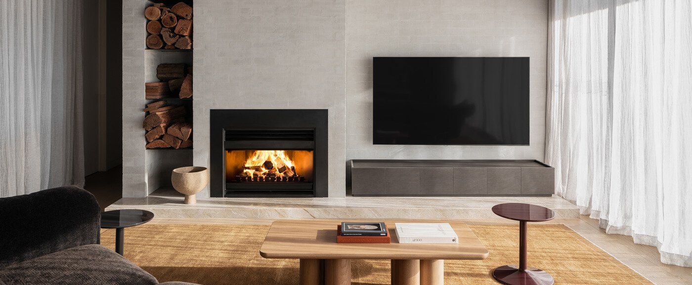 Living Room With a Lit Fireplace, Wall-mounted TV, Coffee Table, and Large Windows — Complete Heating In Huntingfield, TAS