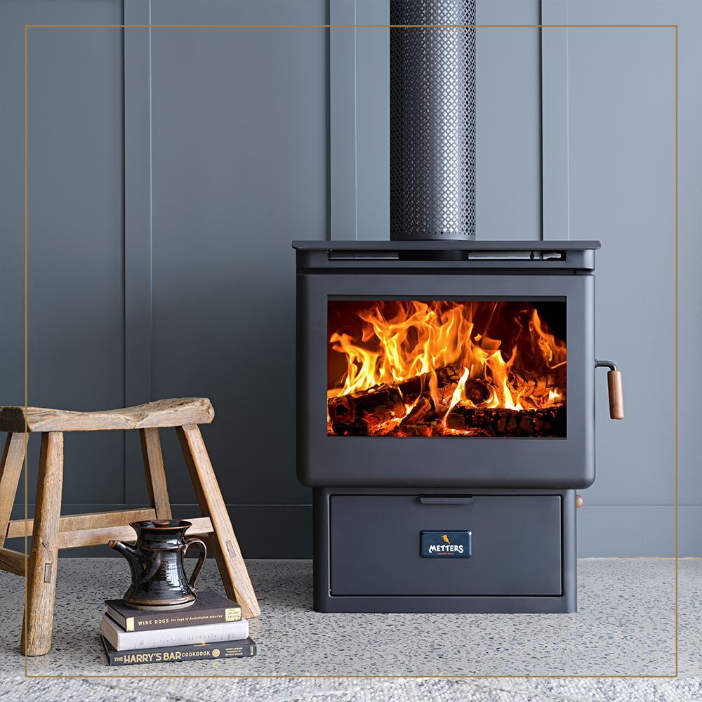 Modern Black Wood Stove With Fire, Grey Wall, Wooden Stool, and Books — Complete Heating In Huntingfield, TAS