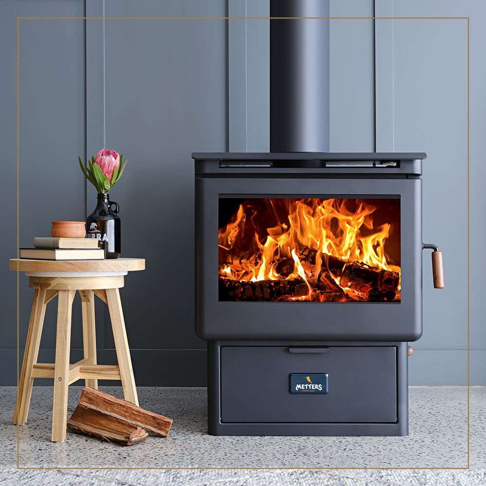 Black Wood-burning Stove With Bright Fire Beside a Small Table and Flowers — Complete Heating In Huntingfield, TAS