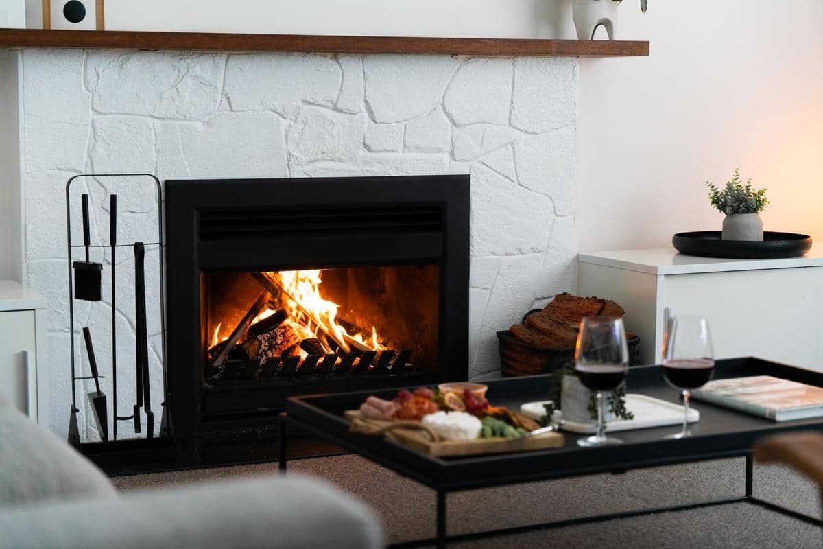 Living Room With a Lit Fireplace, Coffee Table, Wine Glasses, and a Small Plant — Complete Heating In Huntingfield, TAS