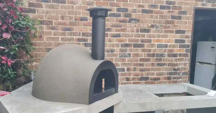 Outdoor Brick Pizza Oven With a Black Chimney on a Patio Against a Brick Wall — Complete Heating In Huntingfield, TAS