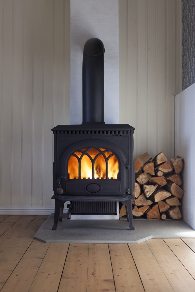 A Black Wood-burning Stove With a Lit Fire Stands on a Stone Hearth — Complete Heating In Huntingfield, TAS