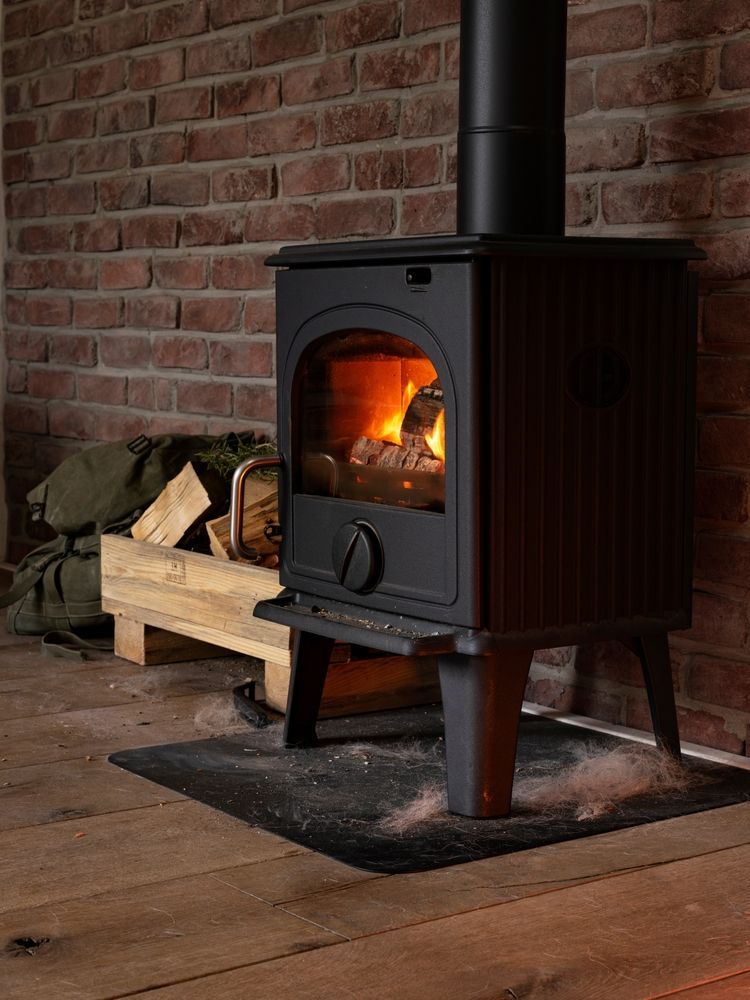 A lit Black Cast-iron Wood Stove Sits on a Hearth Pad — Complete Heating In Huntingfield, TAS