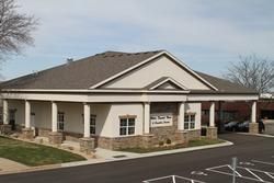 Single-story beige office building with stone base, covered walkway, and parking lot in front