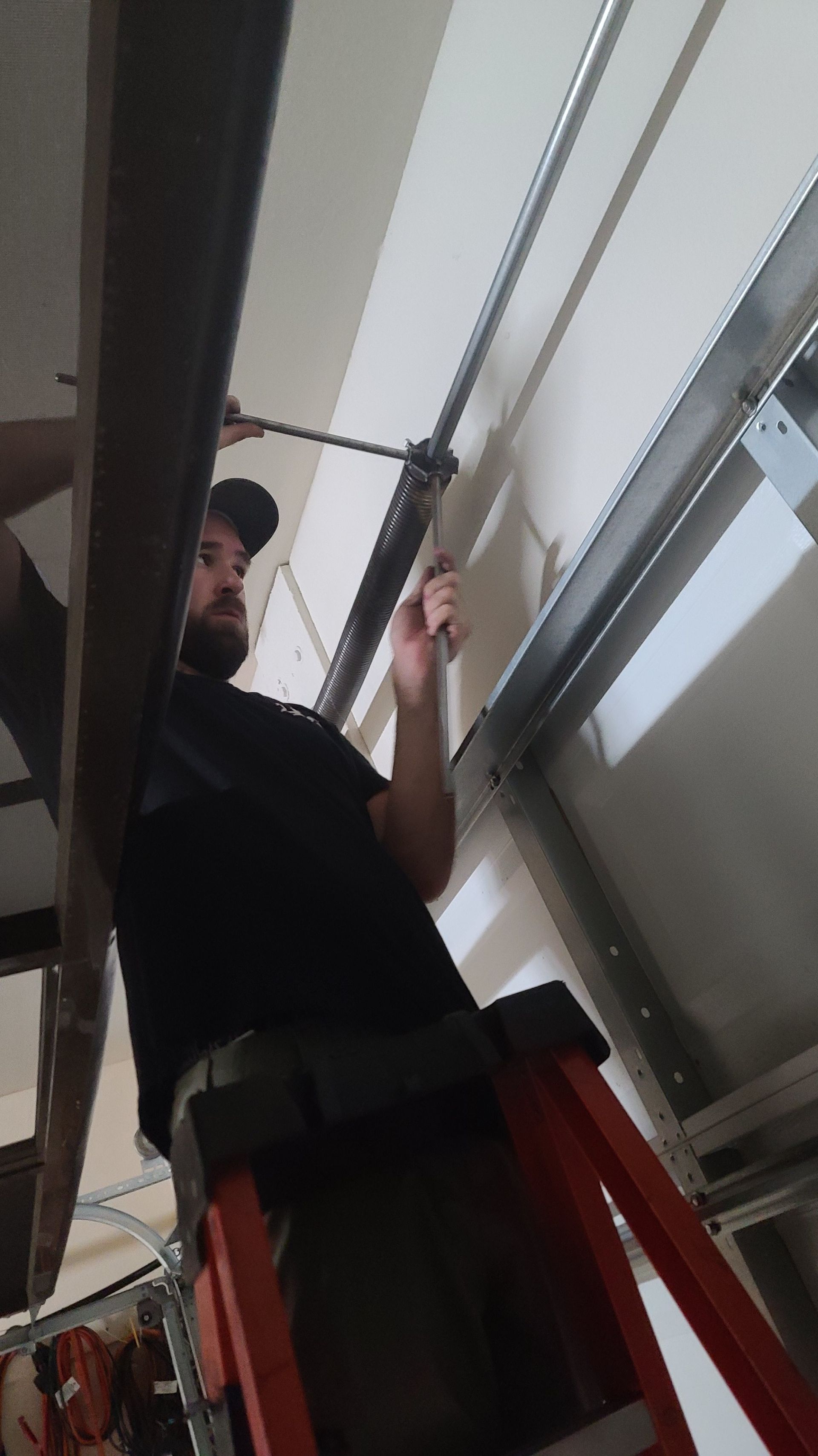 Worker on an orange ladder adjusting a ceiling fixture in a garage-like space.
