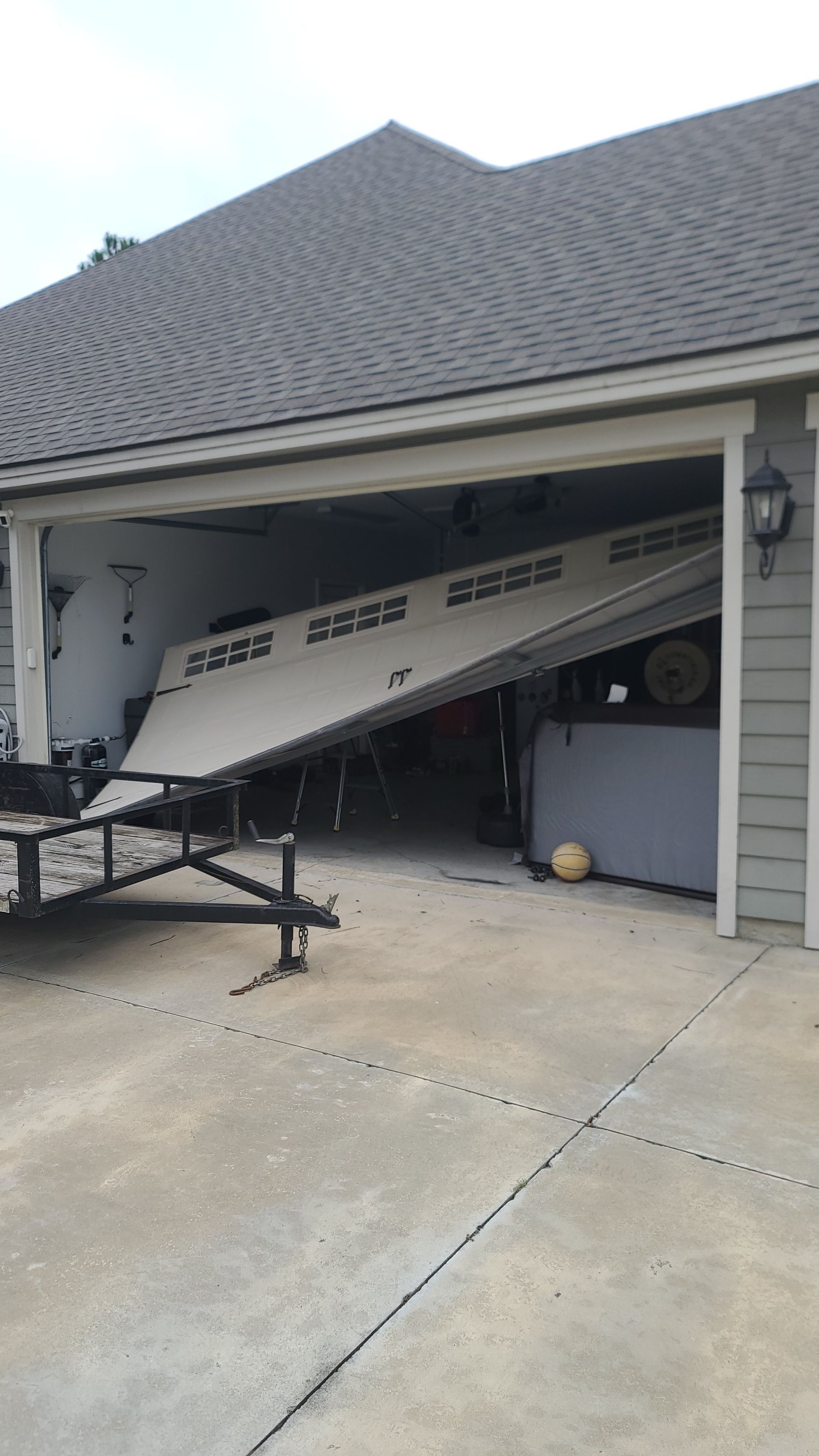Boat stored tilted in a residential garage, with trailer and concrete driveway visible.