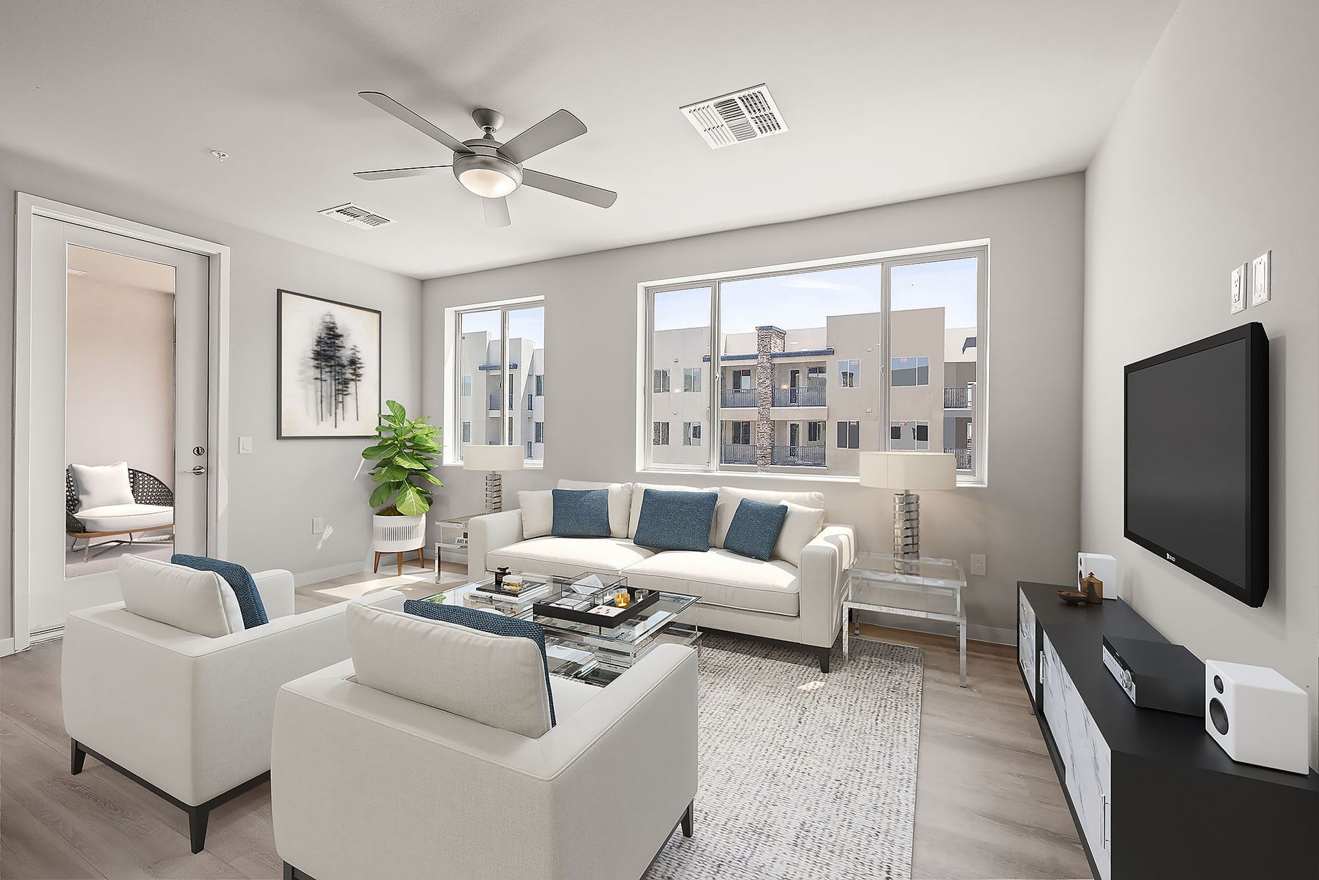 A living room with a couch , two chairs , a television and a ceiling fan.