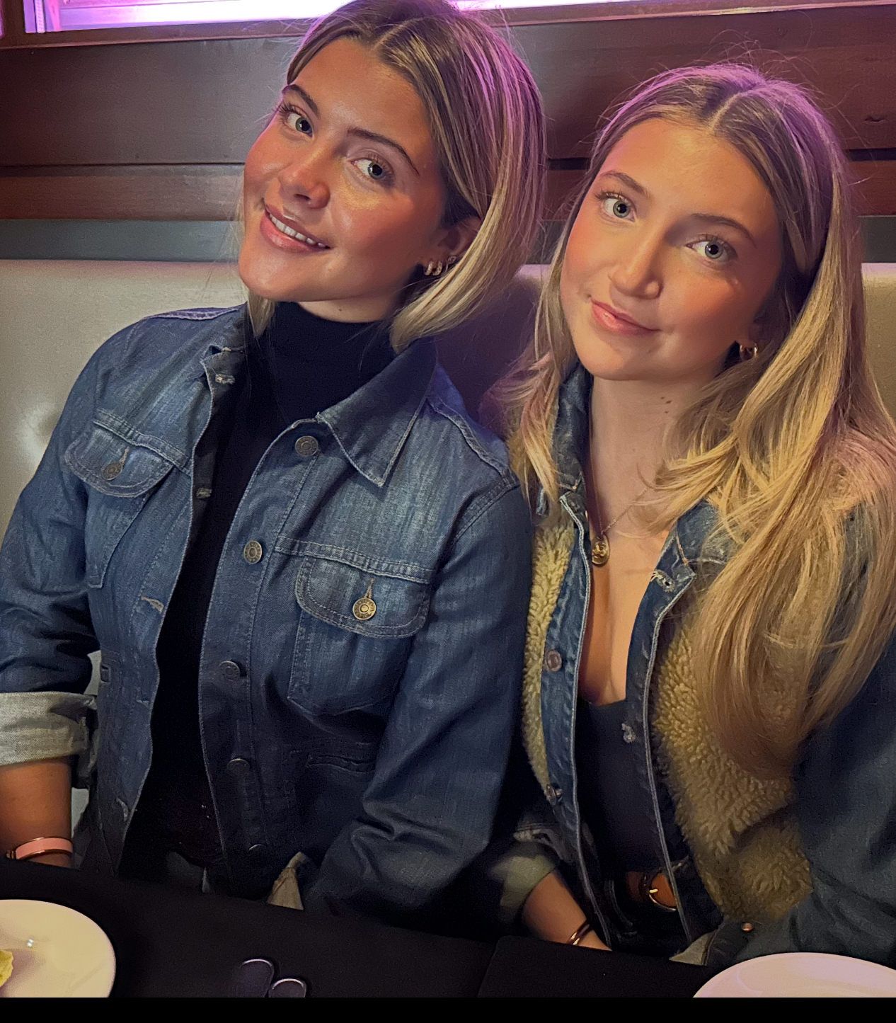 Two people seated side by side in a restaurant booth, smiling at the camera in casual outfits.