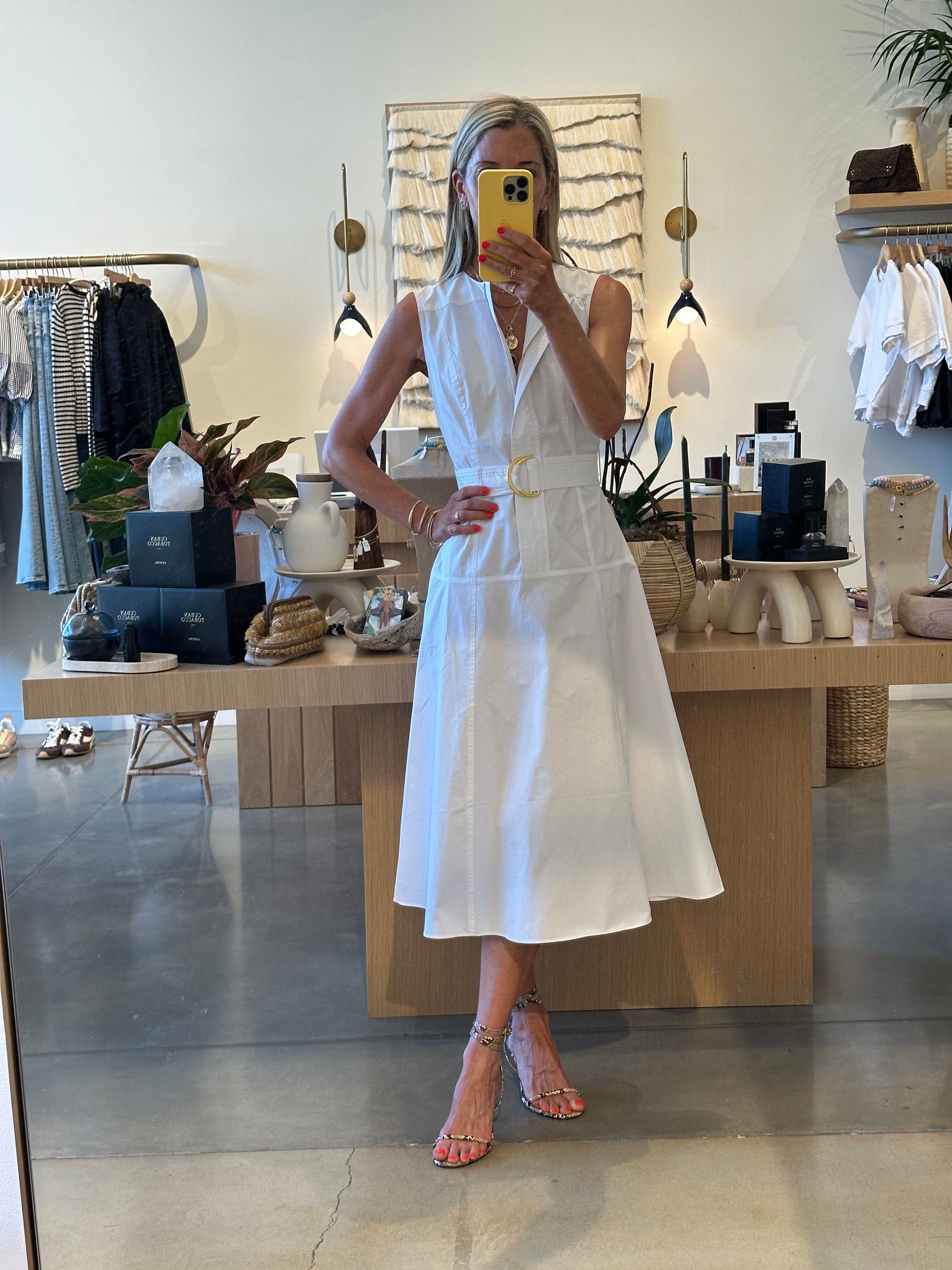 Person in white dress taking a mirror selfie in a clothing boutique