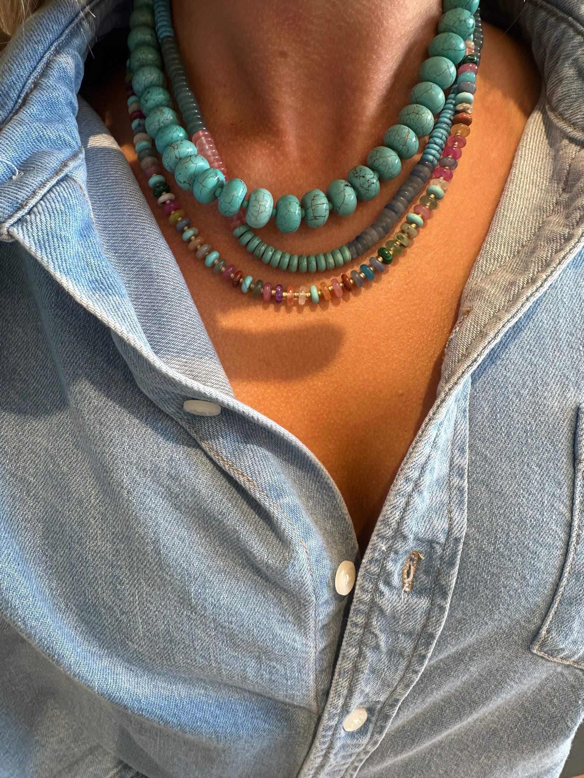 Person wearing layered turquoise and beaded necklaces with an open denim shirt.