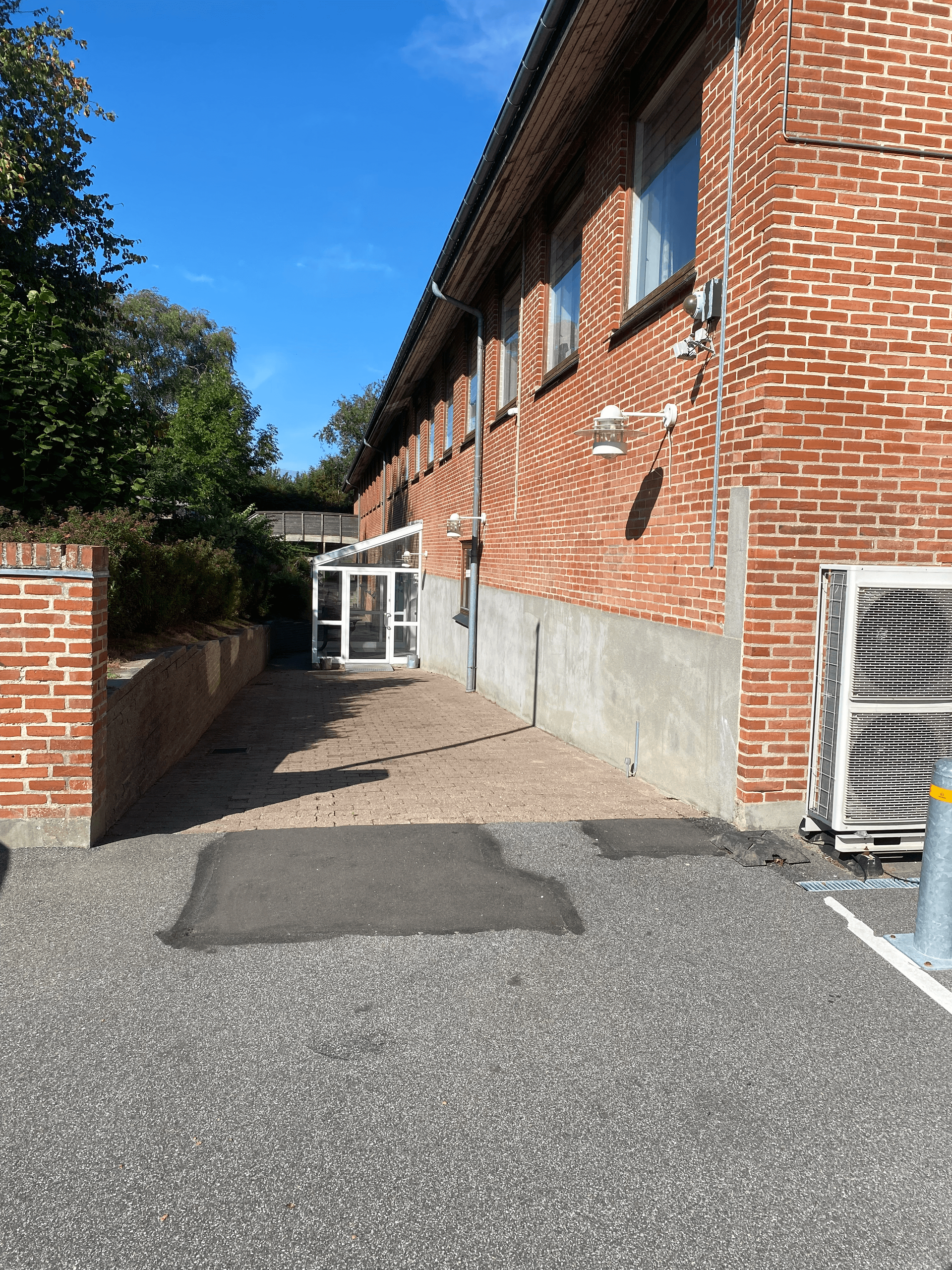 Rød murstensbygning med en grussti, der fører til en glasindhegning. En murstensvæg er til venstre.