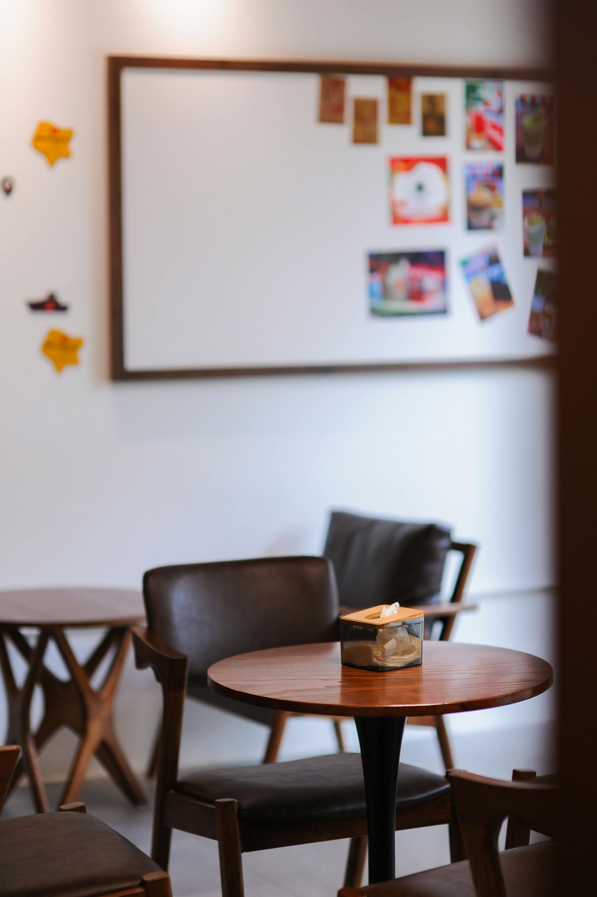 Café-siddeområde: rundt bord med en glaskrukke, stole og en whiteboard med fotos på væggen.