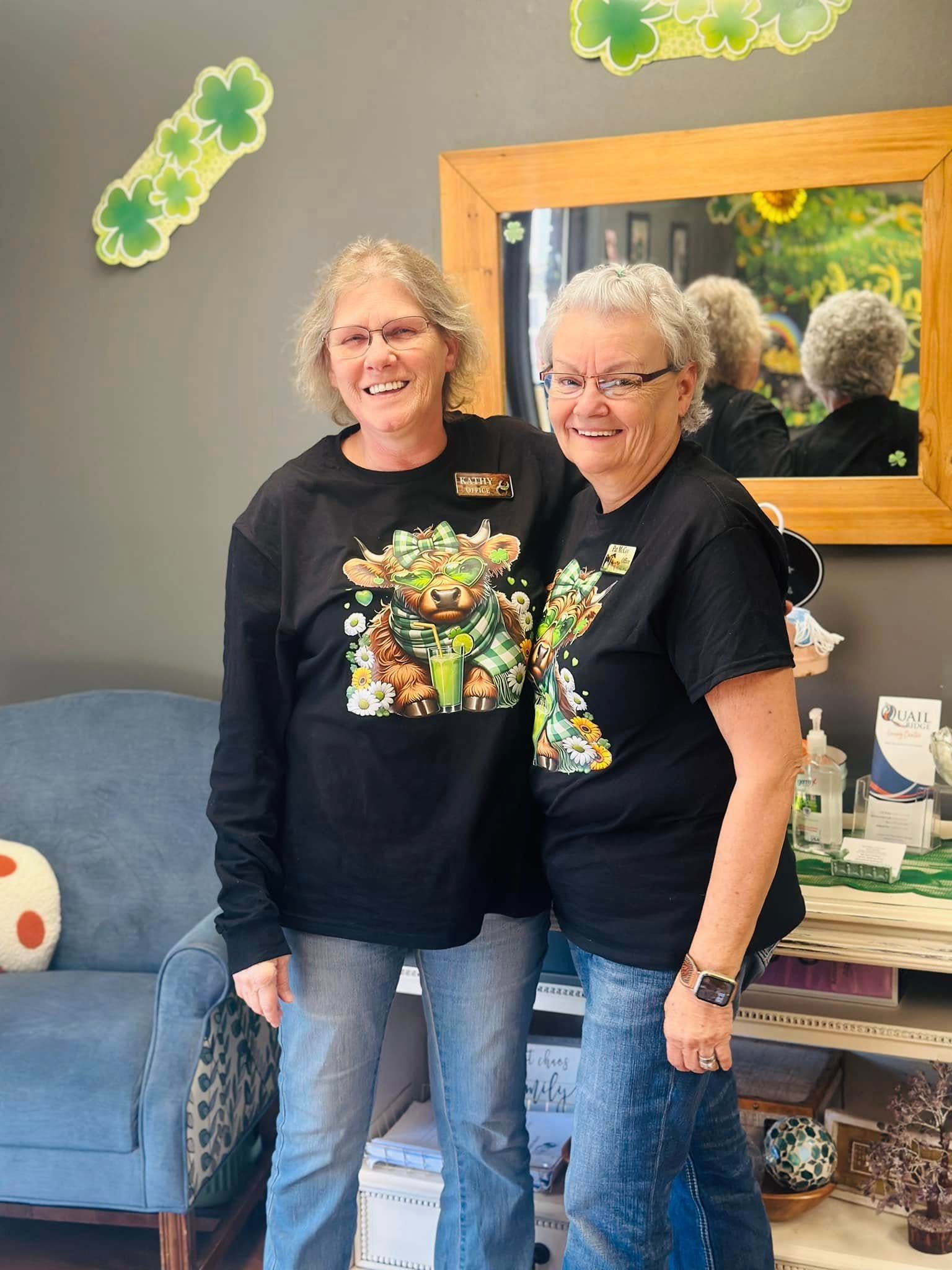 Two women in St. Patrick's Day shirts, one smiling, posing indoors near a mirror.