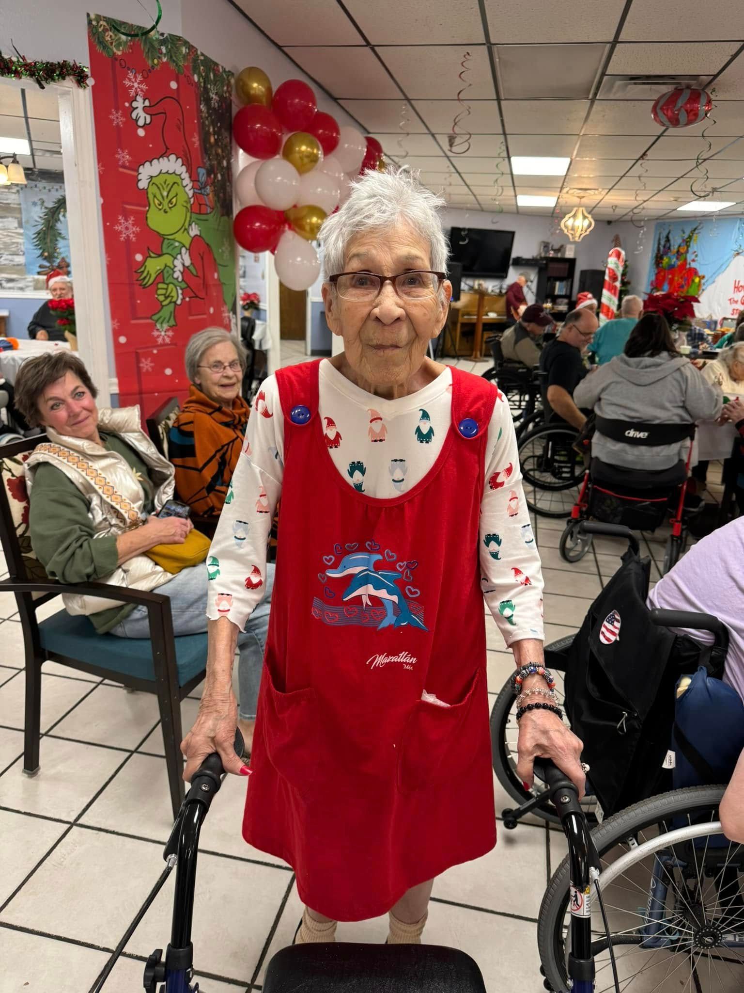 Elderly woman in red jumper, using a walker, smiles at a Christmas gathering.