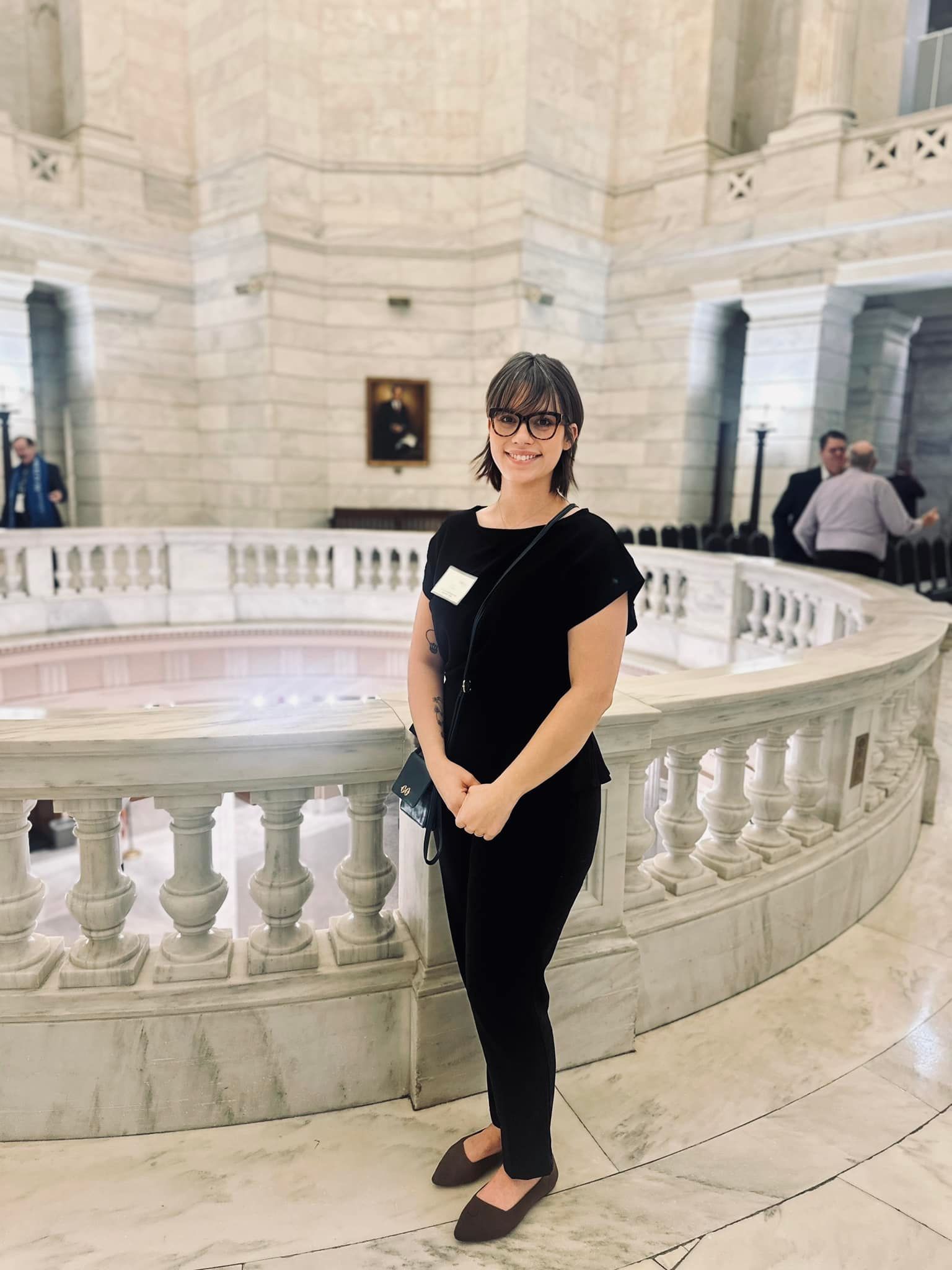Woman in black outfit smiles inside a white marble building.