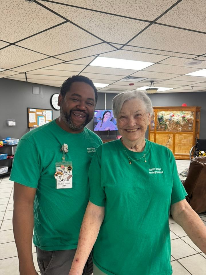 Two people in green shirts smiling at the camera indoors.