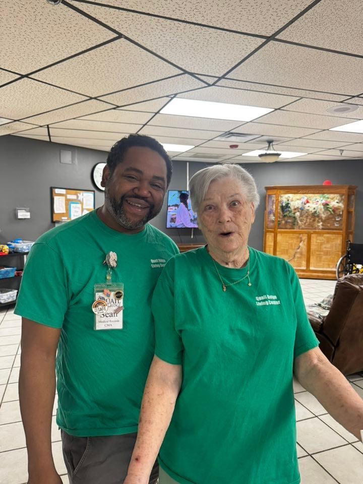 Two people wearing green shirts smile; one male, one female, indoors.