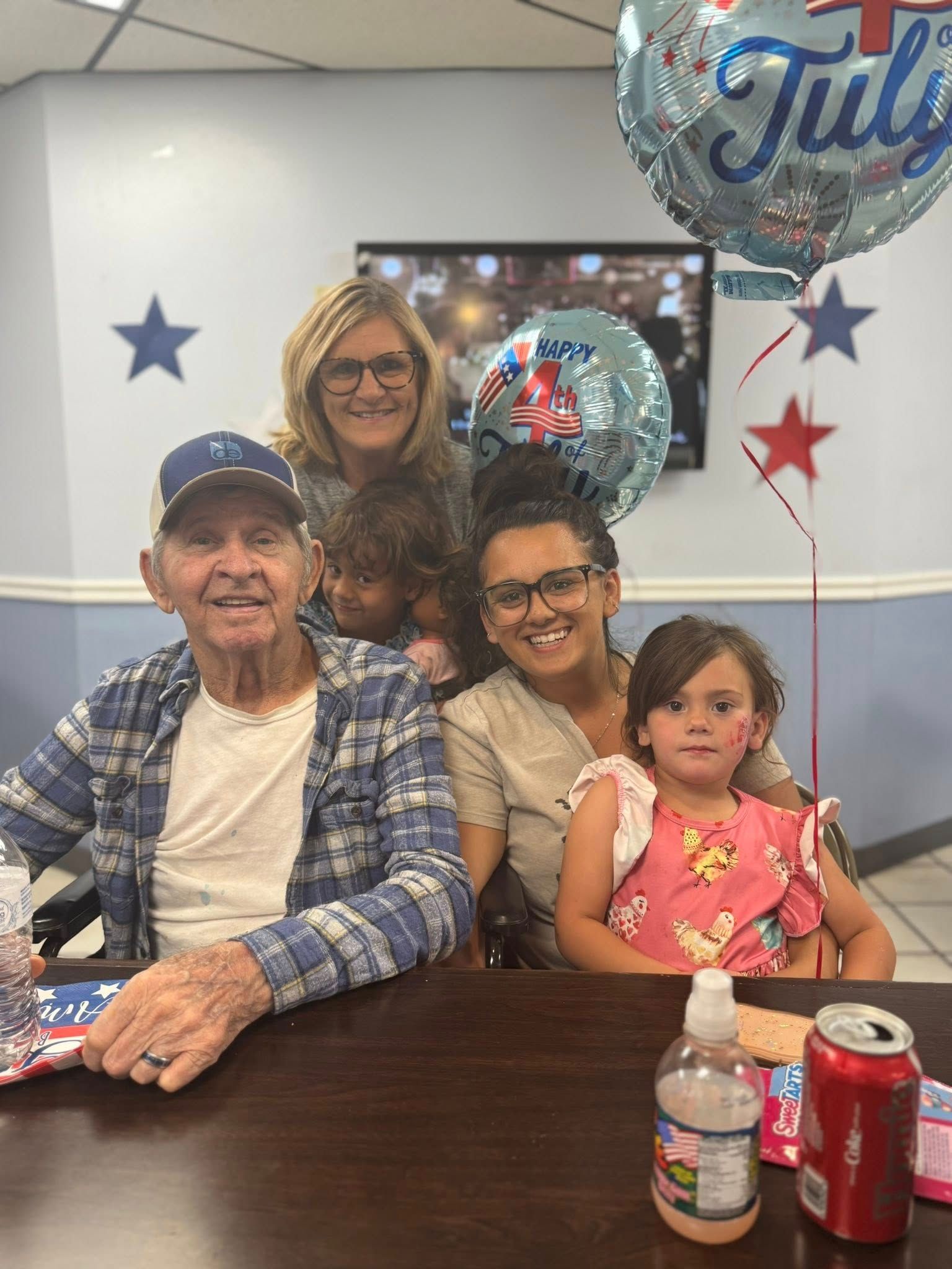 Family celebrating July 4th: man in plaid shirt, woman, two children, & a July balloon.