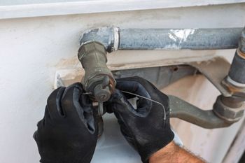 Gloved hands tightening a valve on gray metal pipes against a white wall Gloved hands tightening a valve on gray metal pipes against a white wall