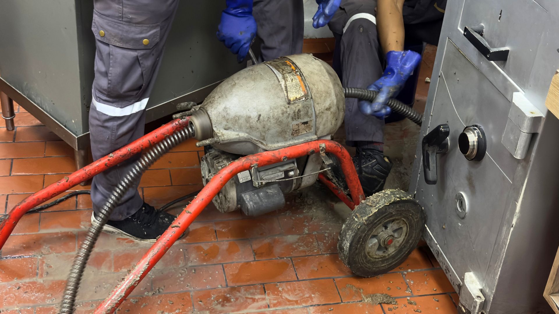 Workers moving a red hose-connected gas cylinder on a wheeled cart in a wet industrial area Workers moving a red hose-connected gas cylinder on a wheeled cart in a wet industrial area