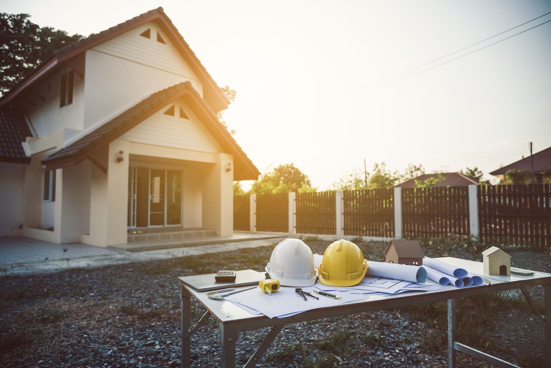 Construction helmets and tools on a table outside a new house at sunset Construction helmets and tools on a table outside a new house at sunset