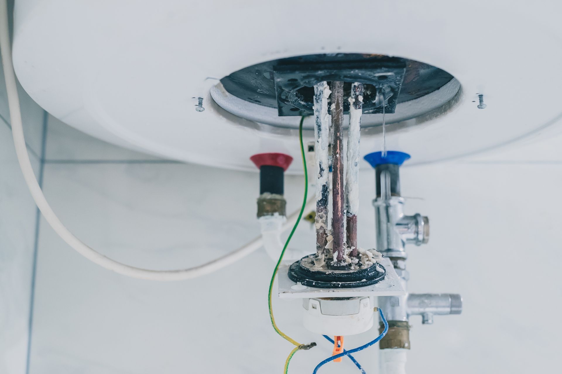 Exposed plumbing and pipes under a sink, with red and blue valves and visible wiring. Exposed plumbing and pipes under a sink, with red and blue valves and visible wiring.