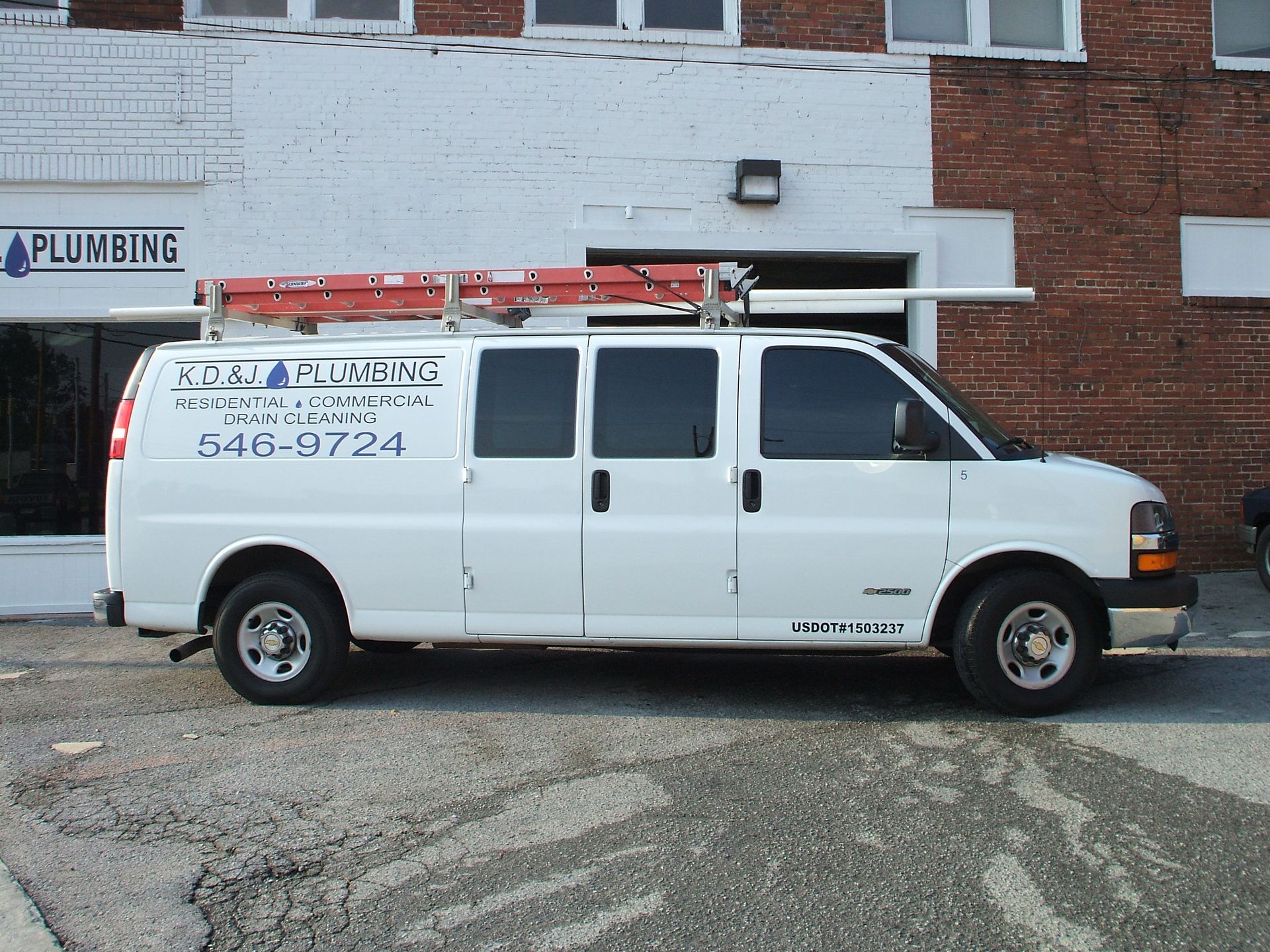 White plumbing service van parked in front of a brick building with a red ladder on top White plumbing service van parked in front of a brick building with a red ladder on top