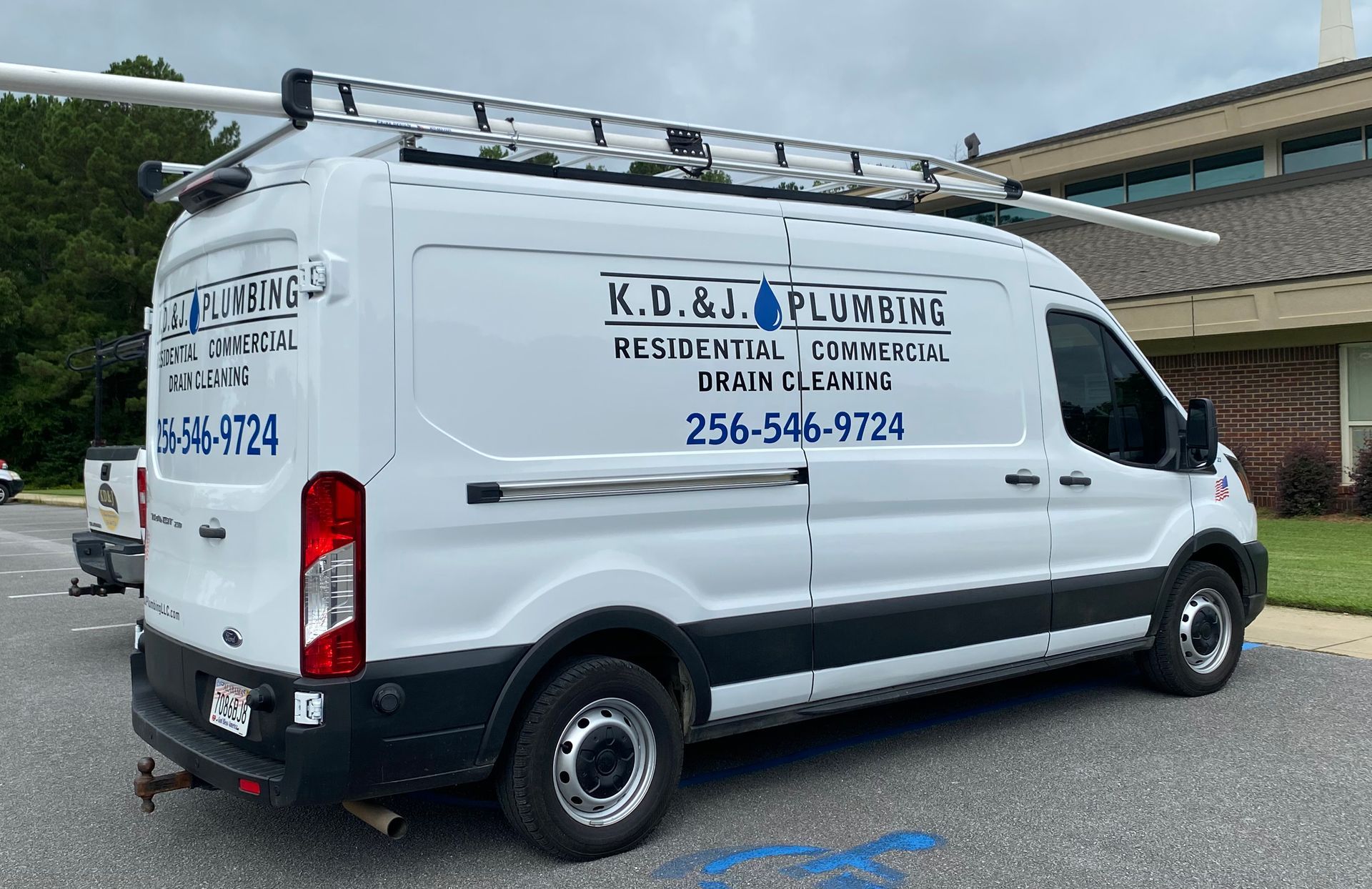 White K.D. & J. Plumbing van parked outdoors, with company logo and phone number on the side.