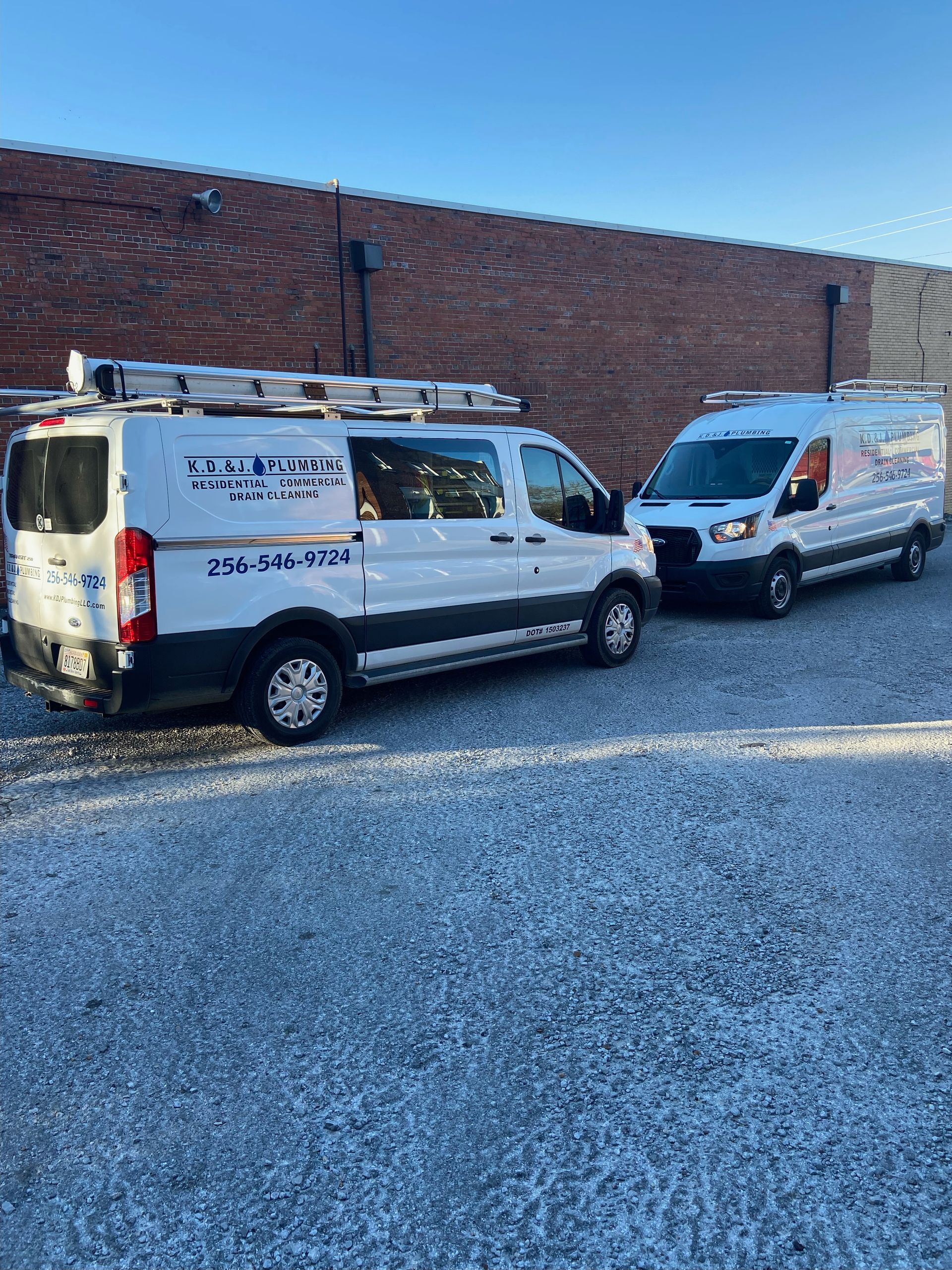 Two white service vans parked on gravel in front of a brick wall under a clear blue sky Two white service vans parked on gravel in front of a brick wall under a clear blue sky
