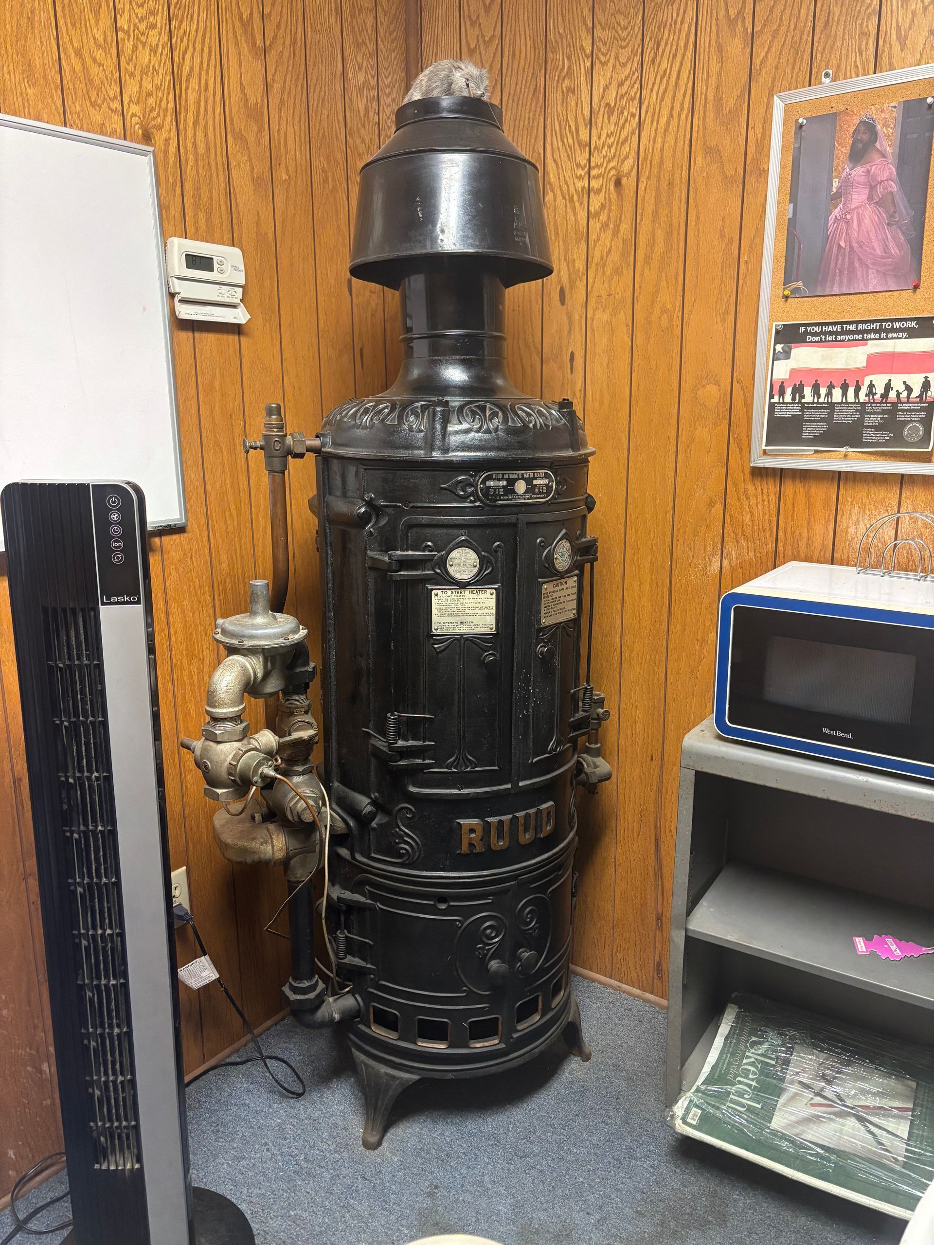 Black vintage cast-iron stove in a wood-paneled room, with shelves and framed posters nearby. Black vintage cast-iron stove in a wood-paneled room, with shelves and framed posters nearby.