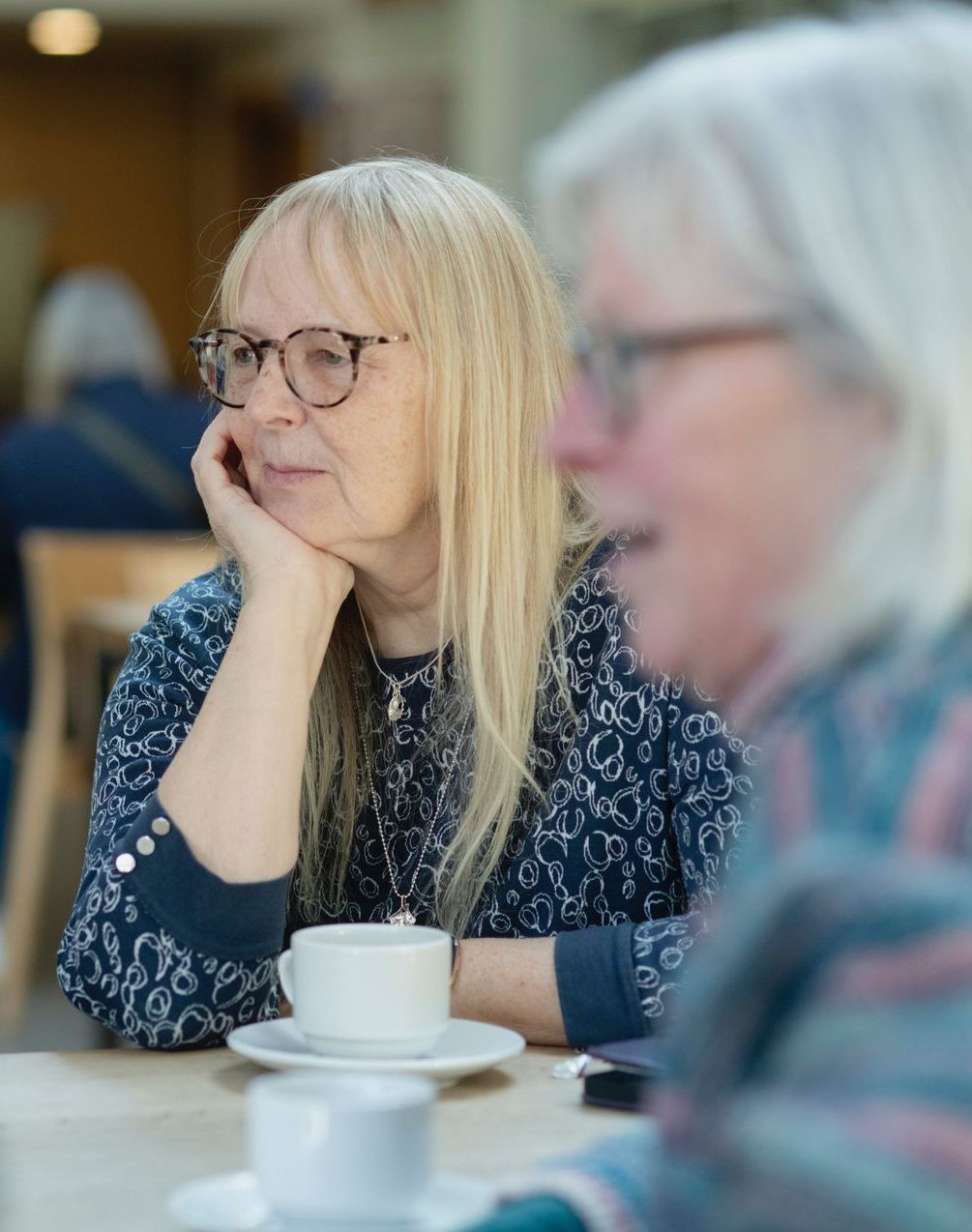 two women are sitting at a table with cups of coffee .