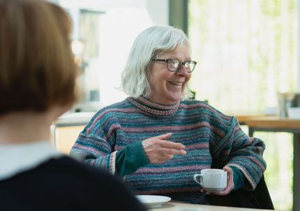 a woman is sitting at a table holding a cup of coffee and smiling .